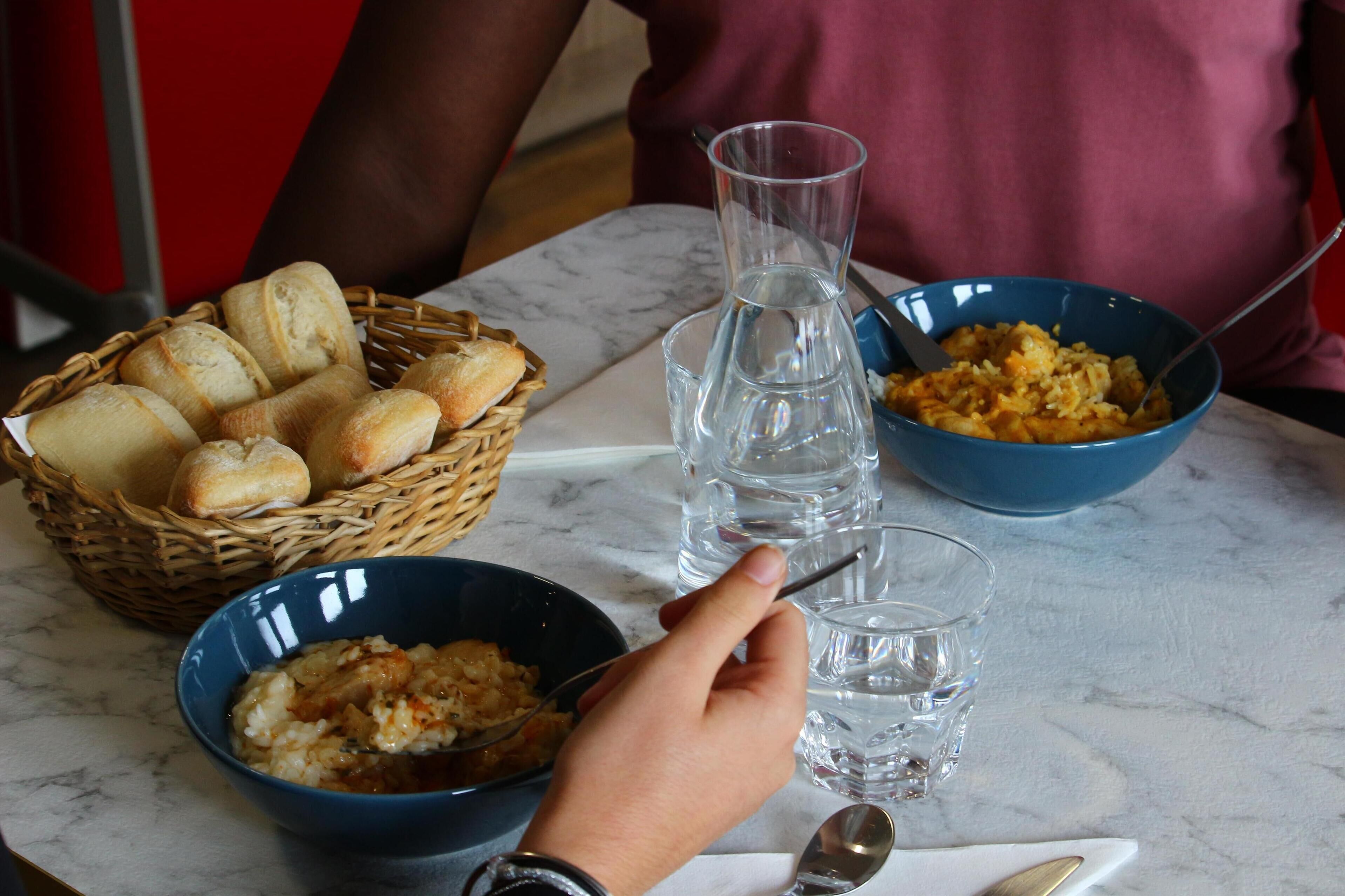 A table with a basket of bread, a bowl of food, a glass of water, and a blue bowl with a spoon.