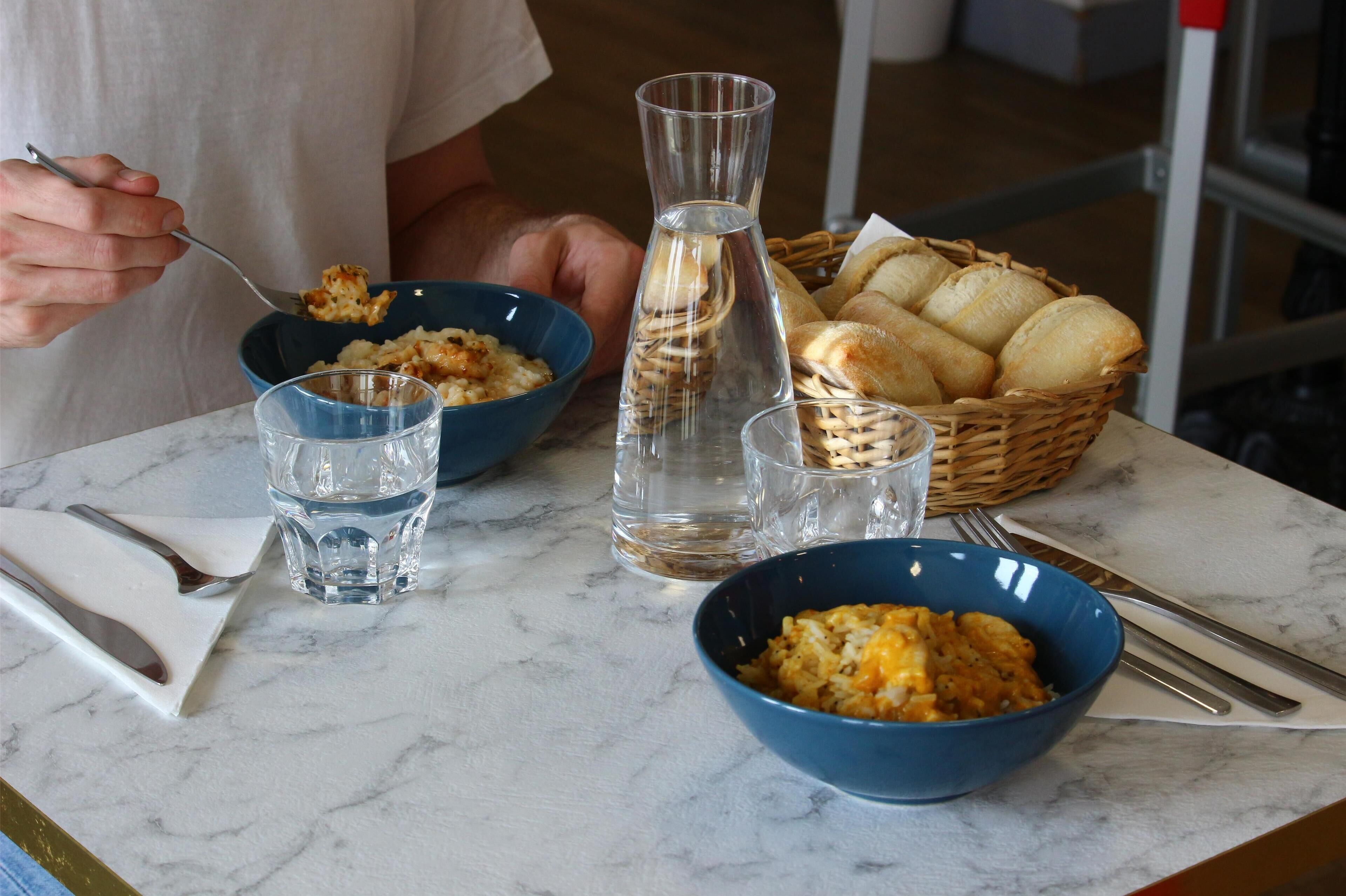 A dining table with two bowls of food, a basket of bread, and a water bottle.