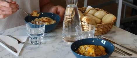 A dining table with two bowls of food, a basket of bread, and a water bottle.