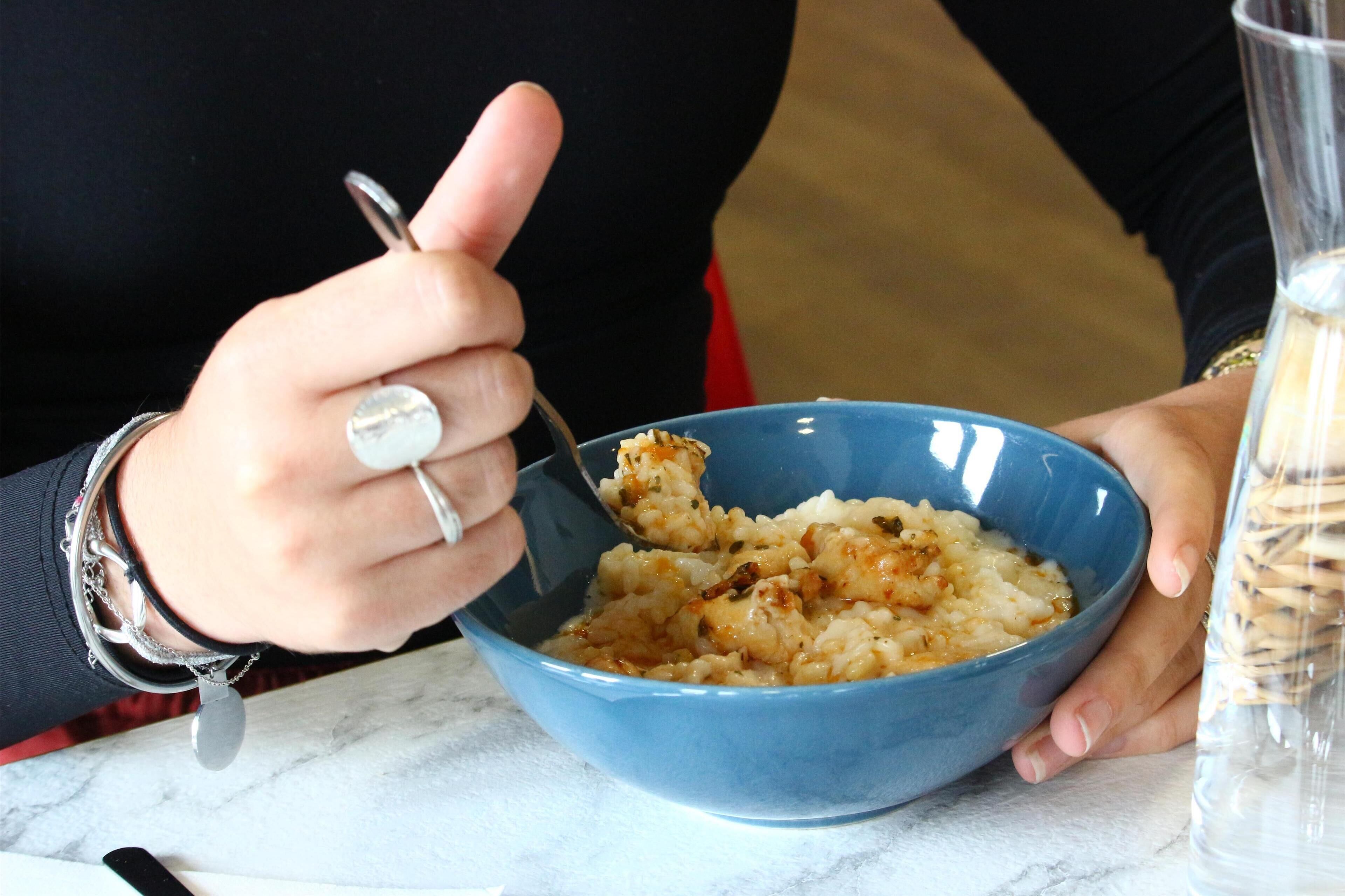 A person holding a blue bowl with a spoon, containing a food item.