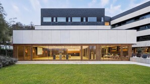 Un edificio moderno con techo plano, amplios ventanales de vidrio y un césped bien cuidado.