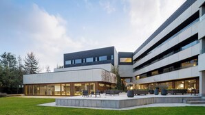 Un edificio moderno con techo plano, amplias ventanas y un patio con zonas de estar.