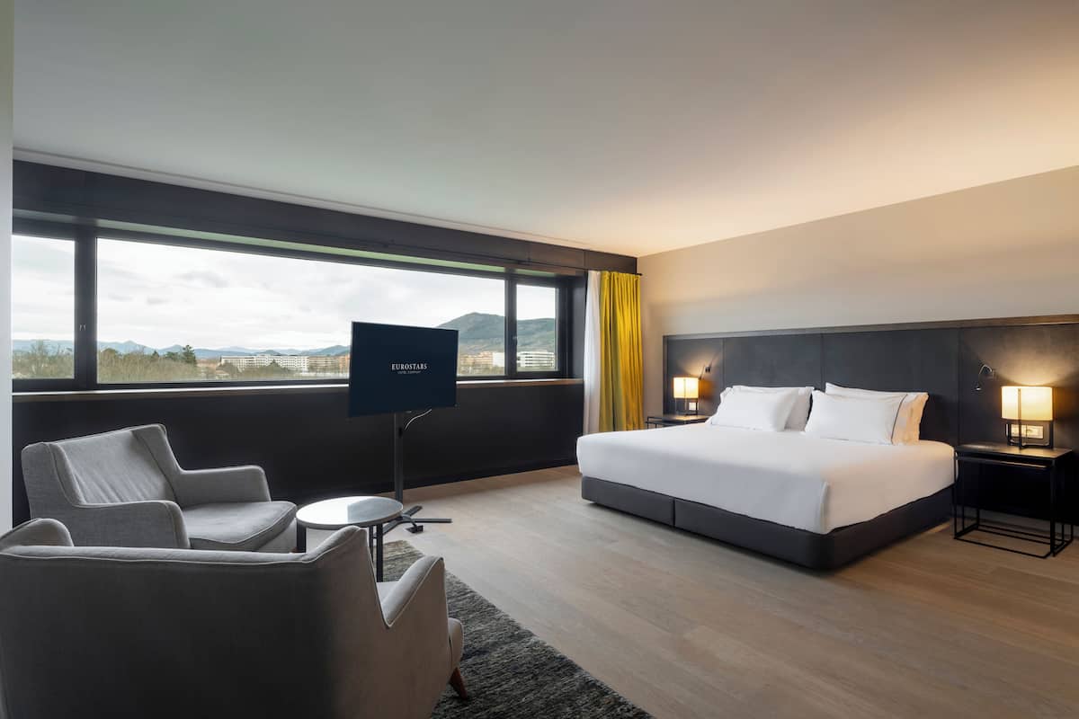 Een moderne hotelkamer met een groot bed, een televisie, een bank en uitzicht op de bergen.