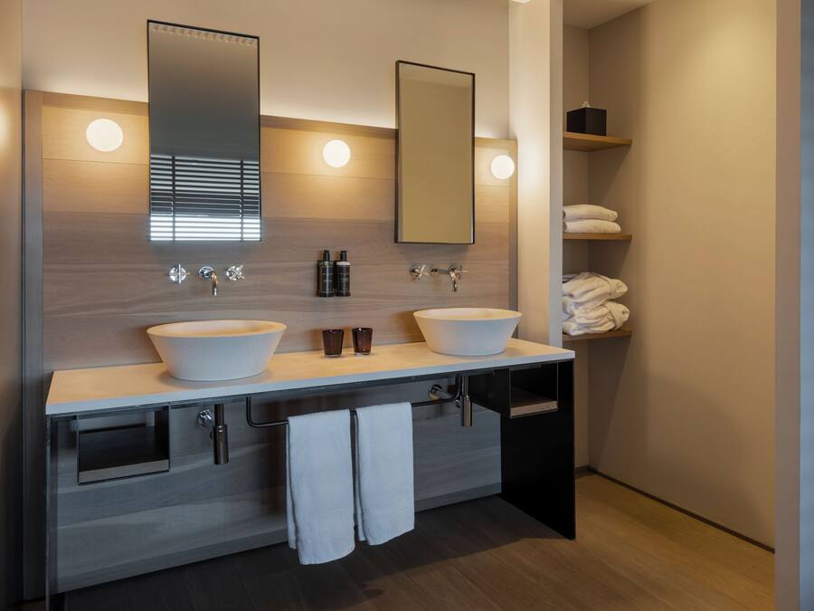 A modern bathroom with two sinks, a large mirror, and built-in shelves with towels.