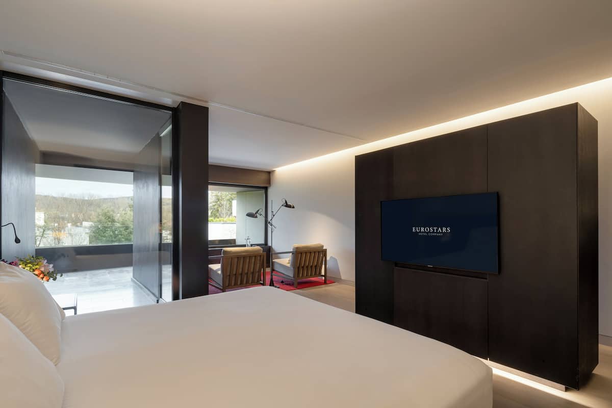 Een moderne hotelkamer met een groot bed, een aan de muur bevestigde televisie en een balkon met uitzicht.