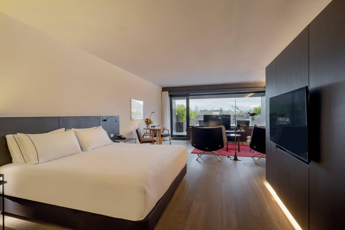 Een moderne hotelkamer met een groot bed, een televisie en een eethoek met een tafel en stoelen.