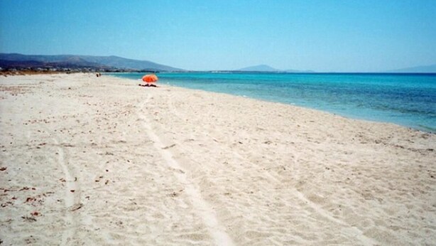 A beach with a clear sky, a sandy shore, and a distant mountain range. - Lianos Studios (Naxos)