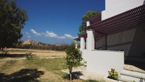 A modern building with a white exterior and a red roof. There is a small tree in front of the building and a clear blue sky in the background. - Lianos Studios (Naxos)