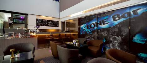 A modern hotel lobby with a bar area, seating, and a large wall mural.
