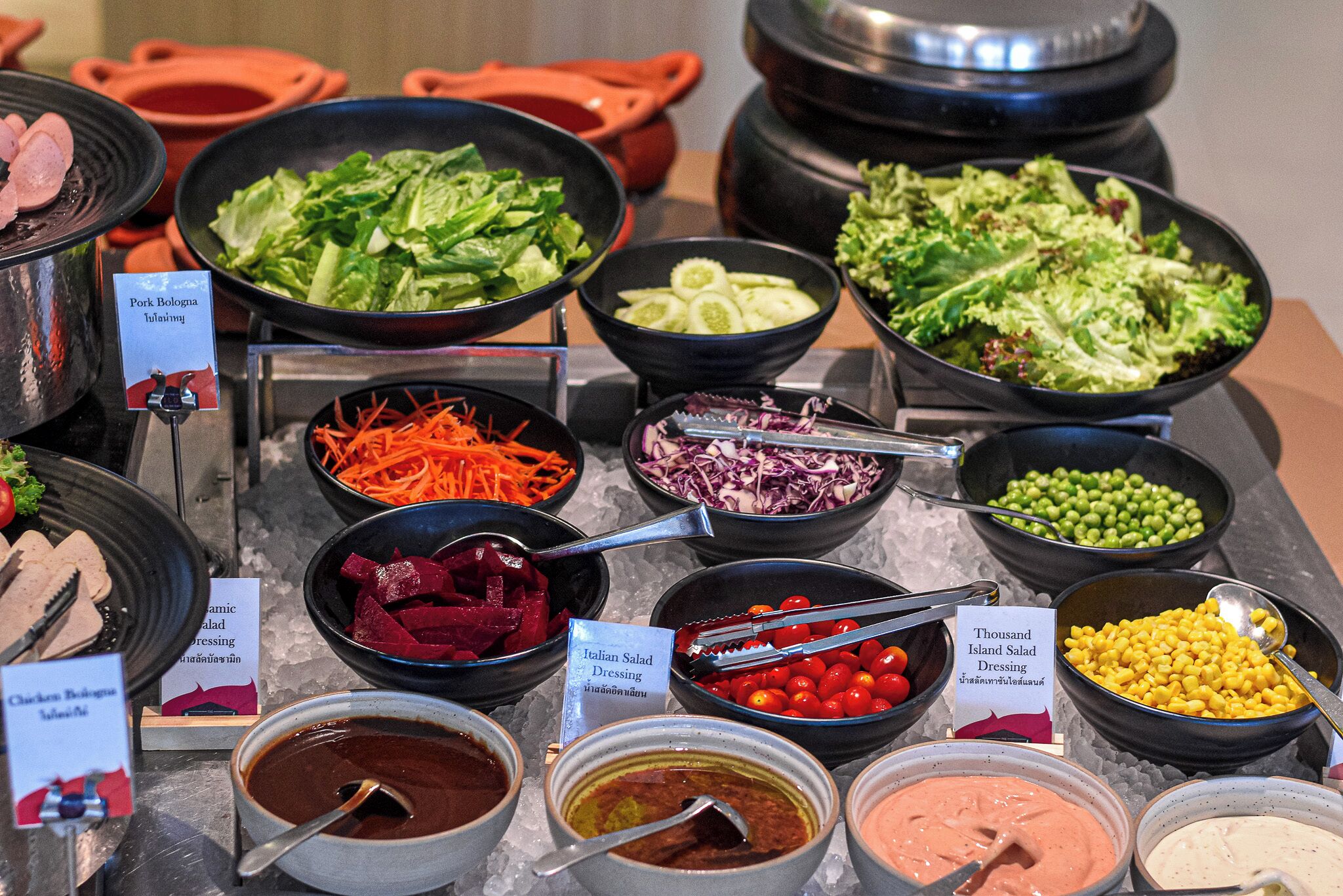 Un bufé con diversas opciones de comida, incluyendo ensaladas, verduras y aderezos.