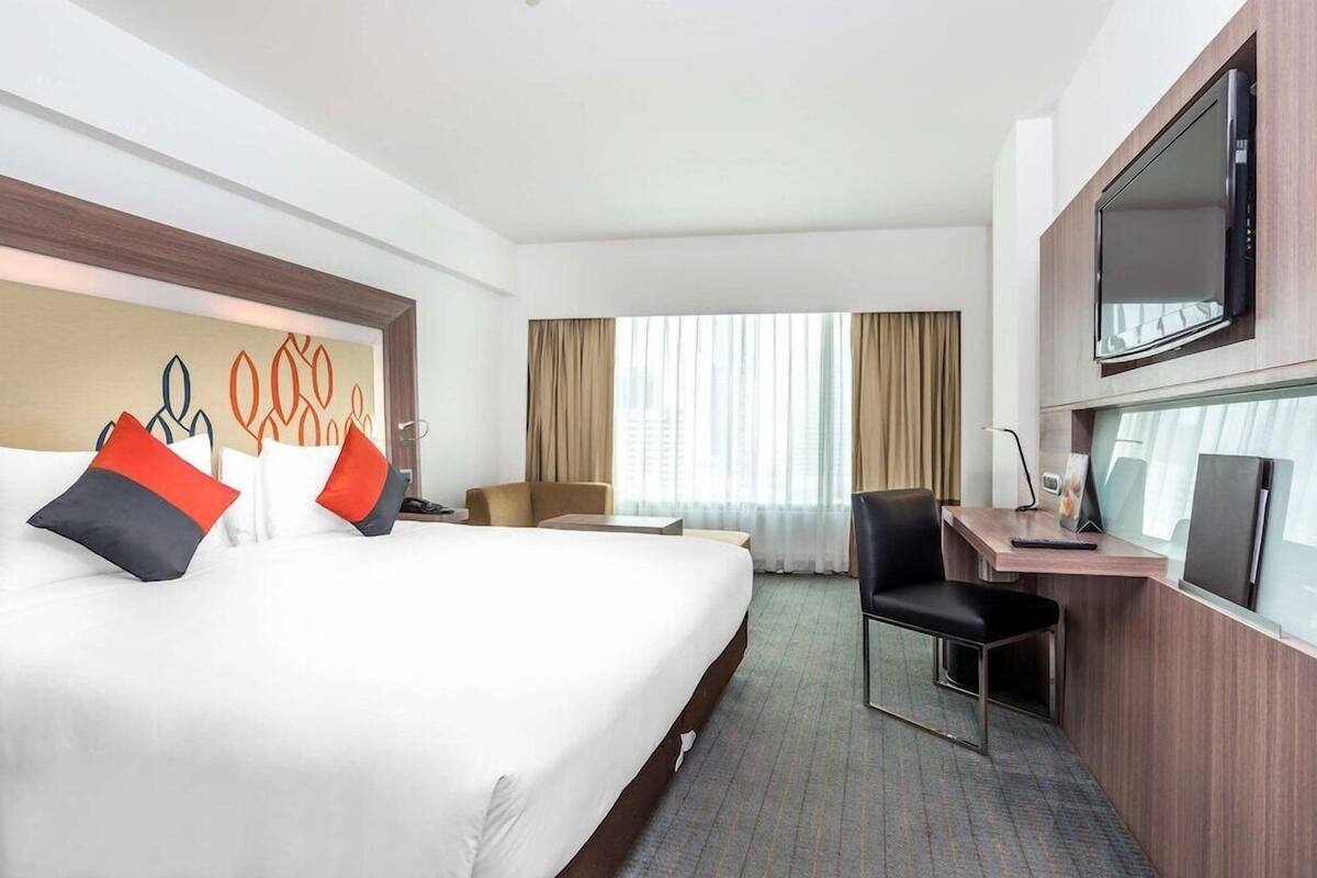 Een hotelkamer met een groot bed, een bureau met stoel, een televisie en een raam met gordijnen.