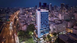 Un hôtel de grande hauteur, reconnaissable à son grand panneau « Hilton Garden Inn », entouré d’immeubles imposants et bordé de rues animées la nuit.