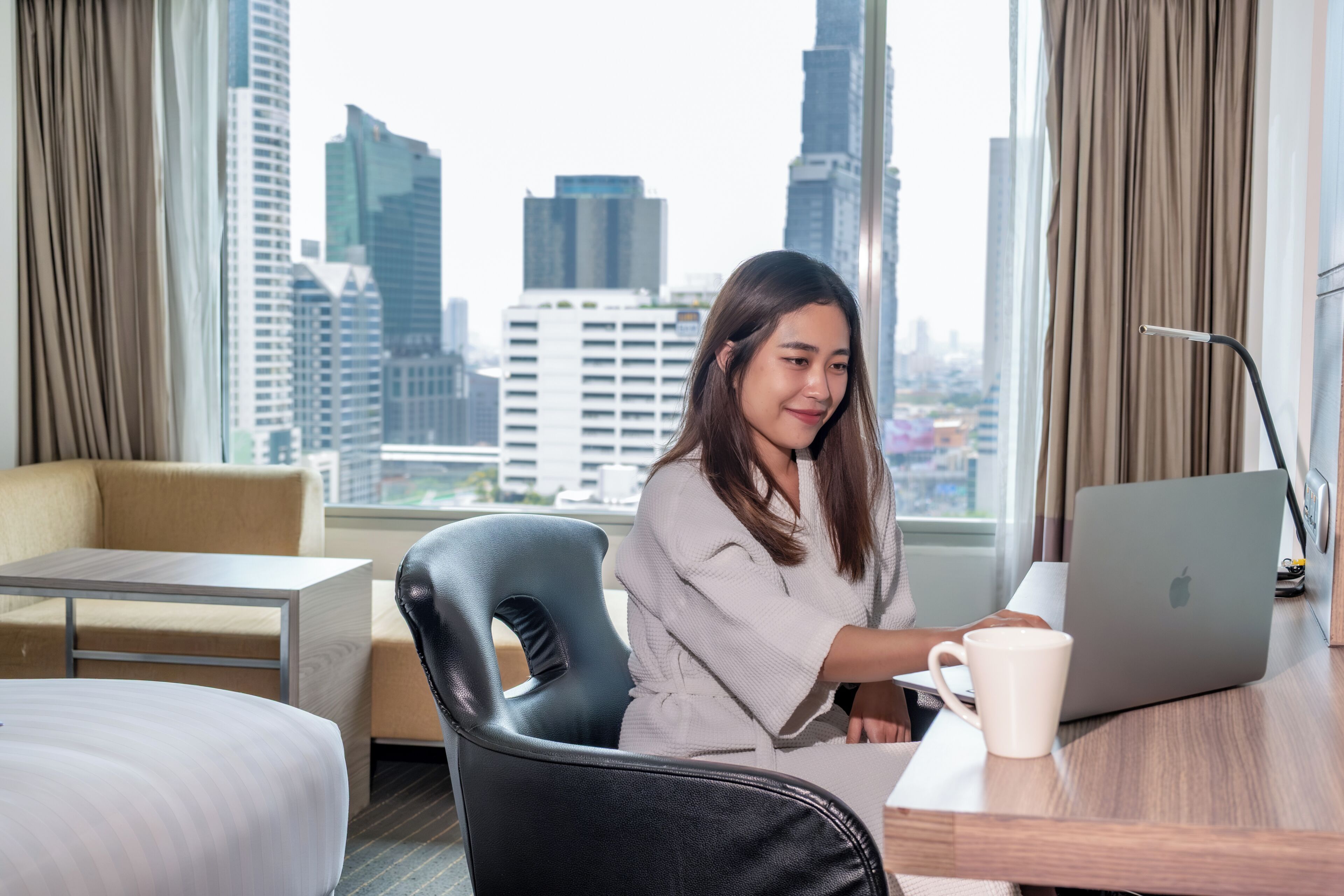 A hotel room with a city view, a desk with a laptop, a chair, and a bed.