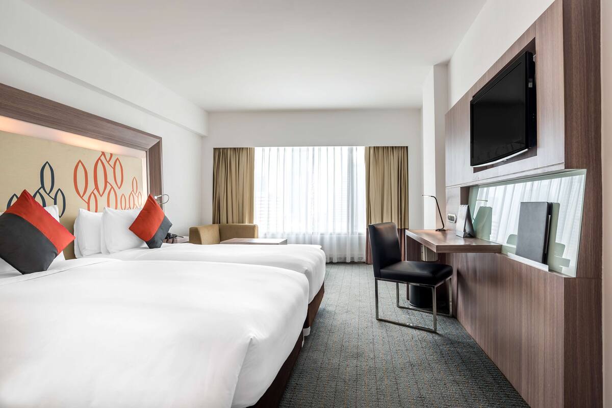 Een hotelkamer met twee bedden, een bureau, een televisie en een raam met gordijnen.
