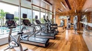 Une salle de sport moderne équipée de tapis de course, d’appareils de musculation et de grandes fenêtres offrant une vue sur la ville.