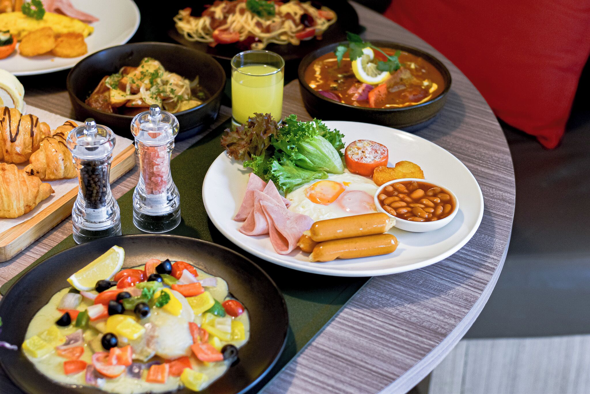 A variety of dishes including a plate with beans, sausages, and vegetables, a bowl of soup, and a plate with eggs and ham.
