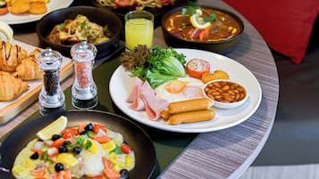 A variety of dishes including a plate with beans, sausages, and vegetables, a bowl of soup, and a plate with eggs and ham.