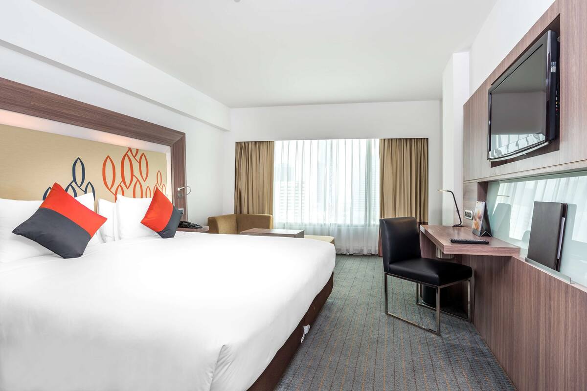Een hotelkamer met een groot bed, een bureau, een stoel, een televisie en een raam met gordijnen.