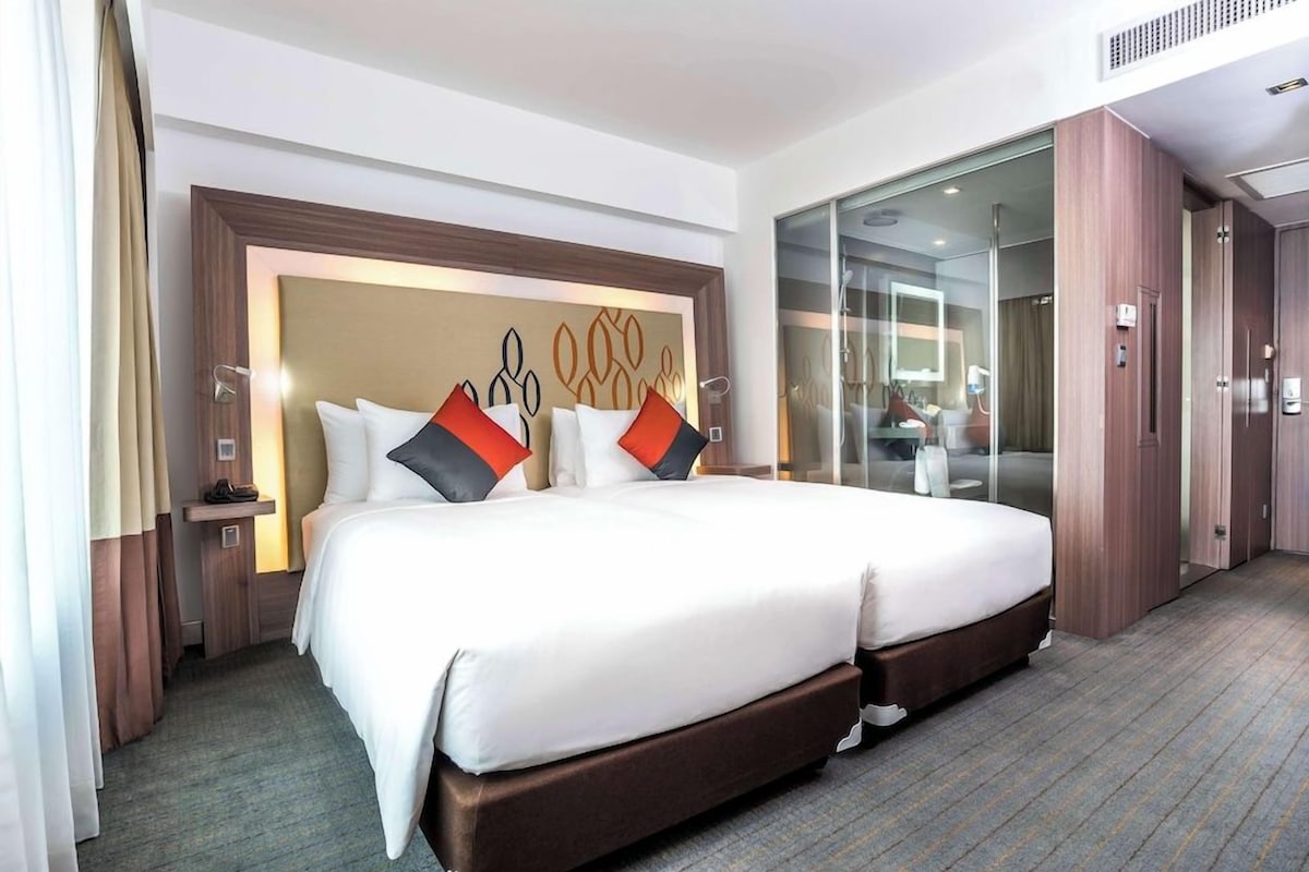 A hotel room with a large bed, a glass partition, and a wooden wardrobe.