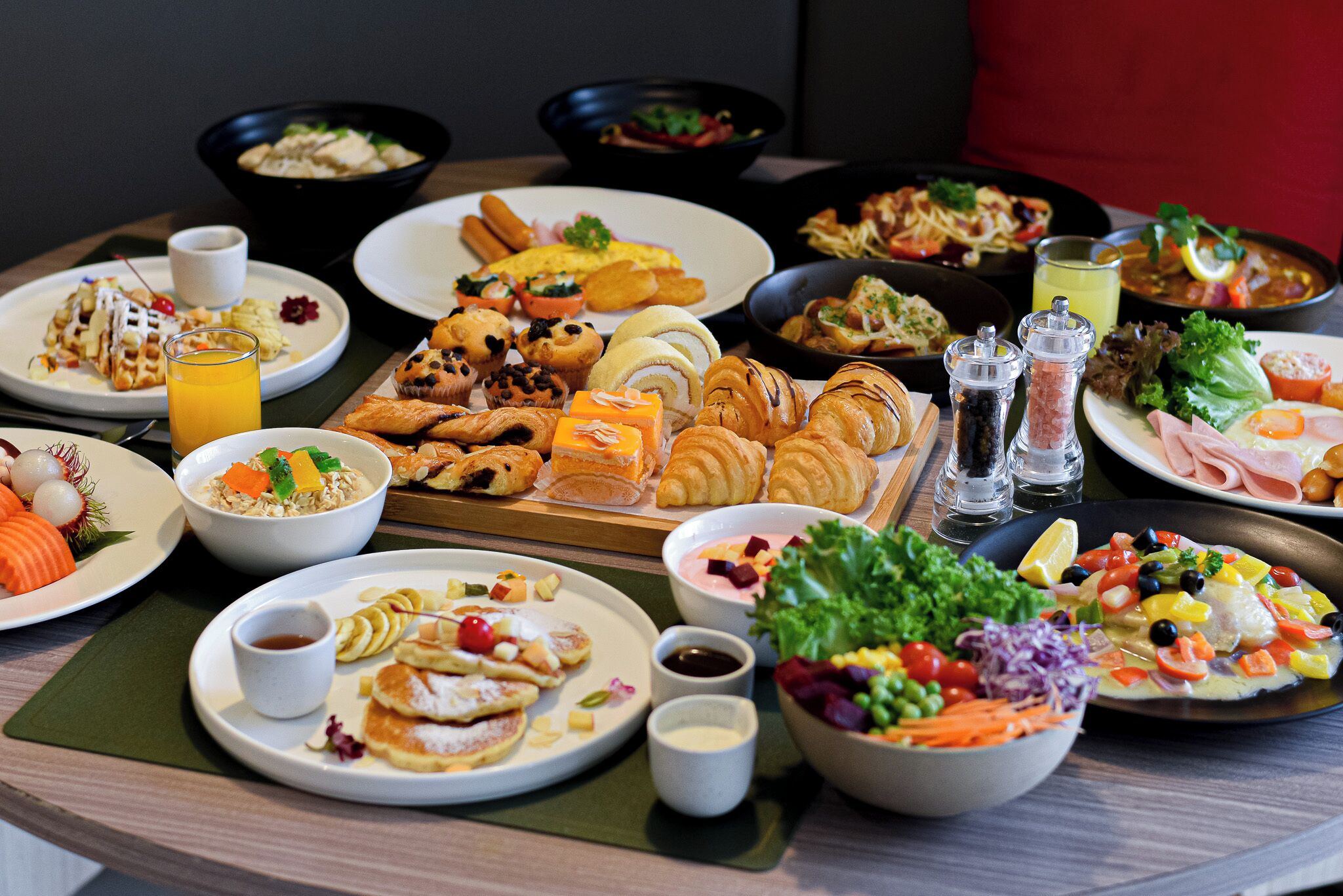 Diversos platos de desayuno sobre una mesa redonda, como panqueques, huevos y pasteles.