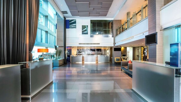Un hall d’hôtel moderne doté d’un comptoir d’accueil, de rampes en verre et d’un aménagement spacieux.