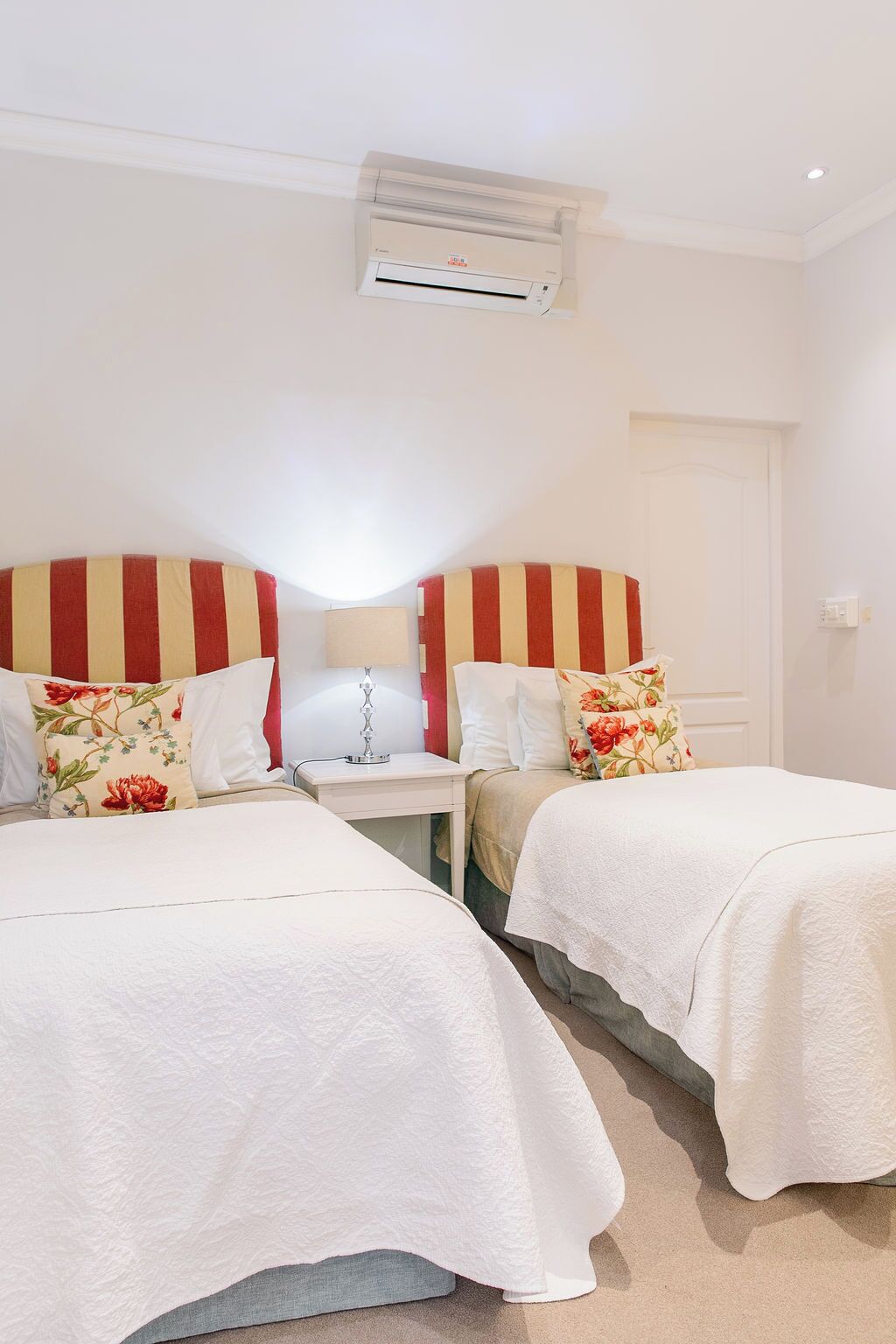 Habitación de hotel con dos camas, una mesita de noche, una lámpara y un equipo de aire acondicionado.