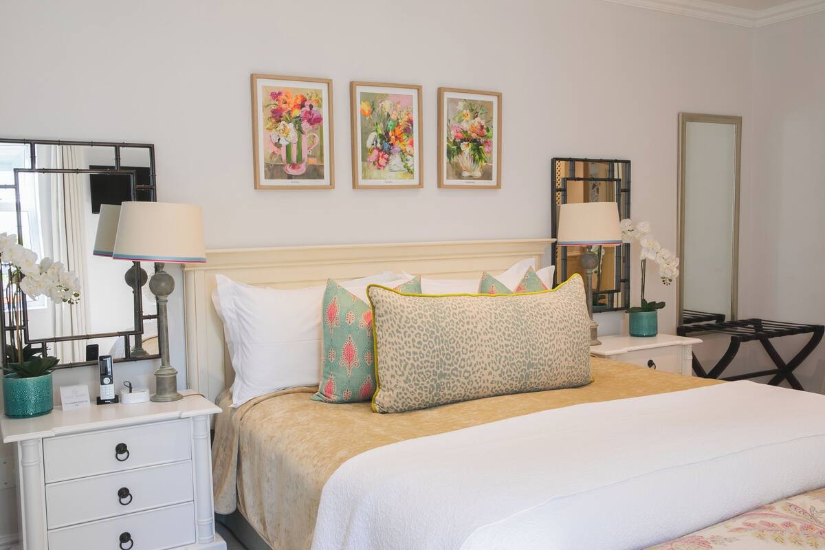 A neatly arranged bedroom with a bed, bedside tables, lamps, and framed floral artwork on the wall.