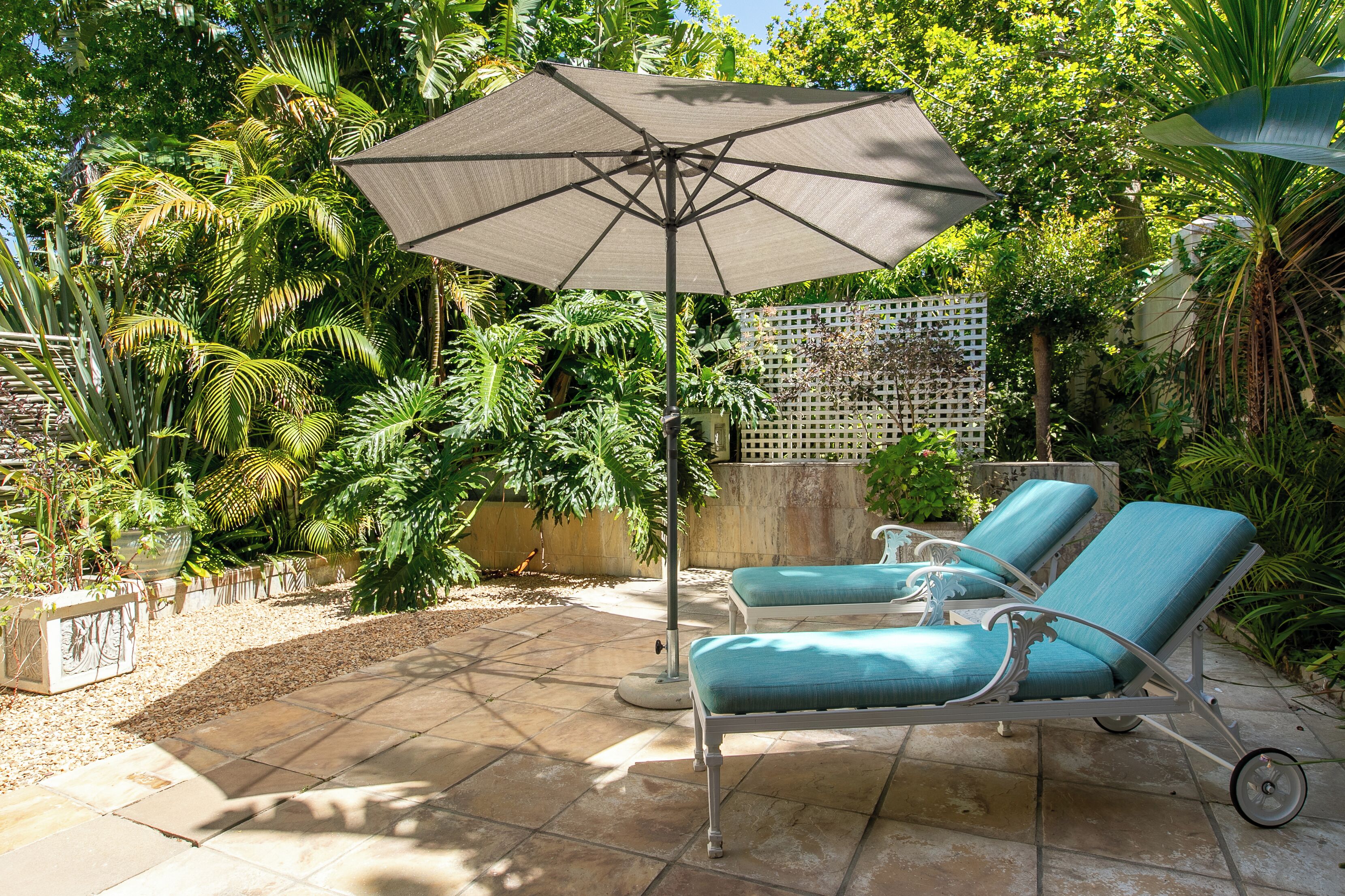 Un patio con dos sillones de descanso y una sombrilla grande, rodeado de exuberante vegetación tropical.