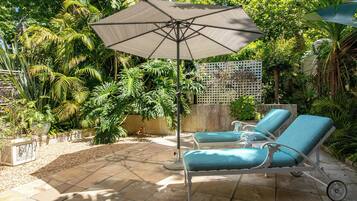 Un patio con dos sillones de descanso y una sombrilla grande, rodeado de exuberante vegetación tropical.
