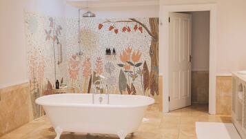 A bathroom with a freestanding bathtub, a shower with a mosaic wall, and a door leading to another room.