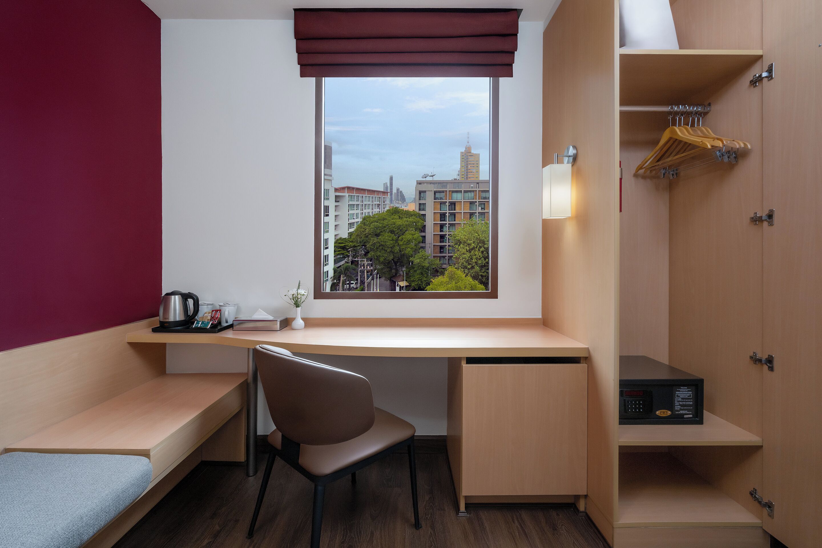 A compact hotel room with a desk, chair, and a view of the cityscape through a window.