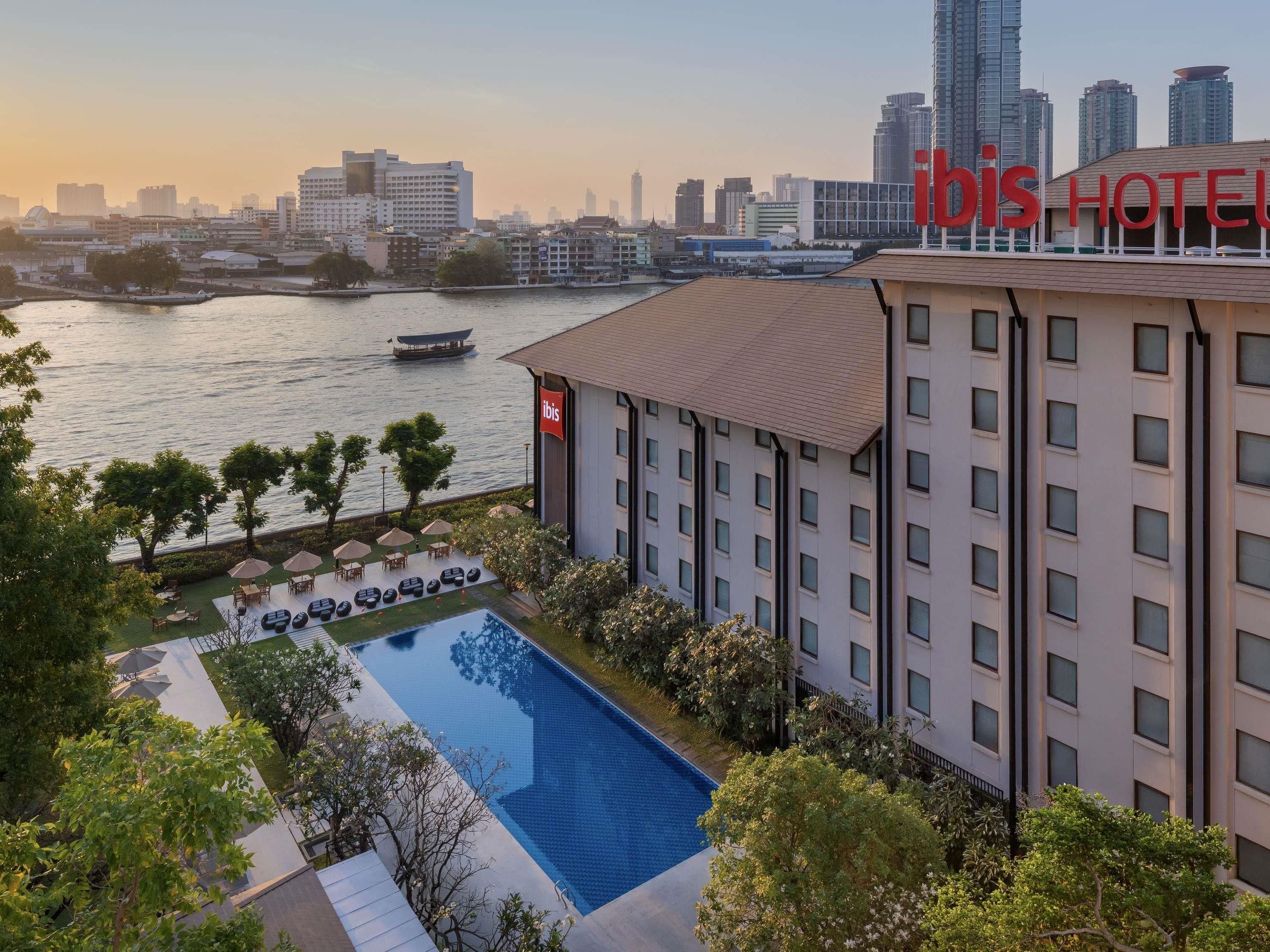 A hotel with a swimming pool, outdoor seating, and a view of the city skyline.