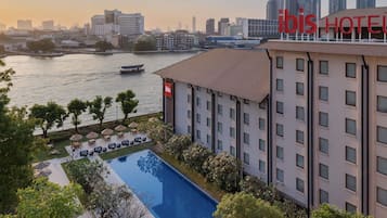 A hotel with a swimming pool, outdoor seating, and a view of the city skyline.