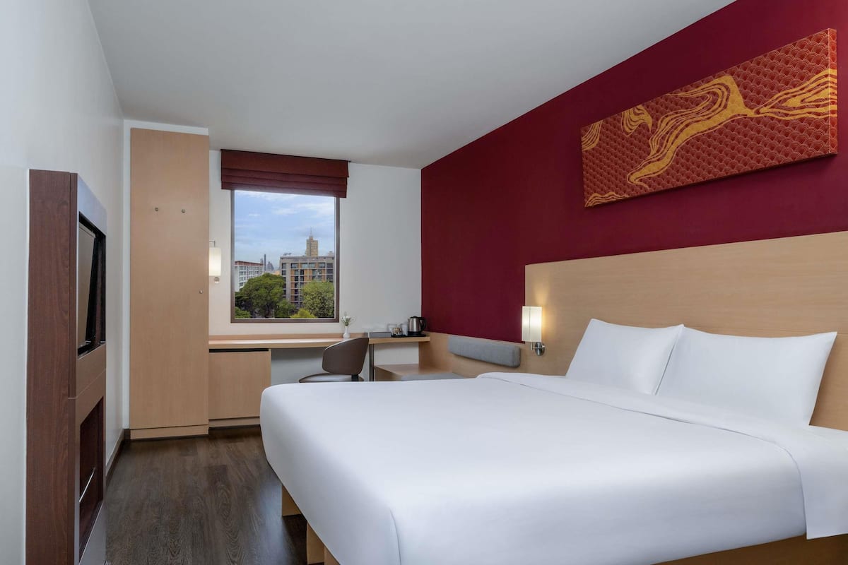 A hotel room with a bed, desk, chair, and a window with a city view.