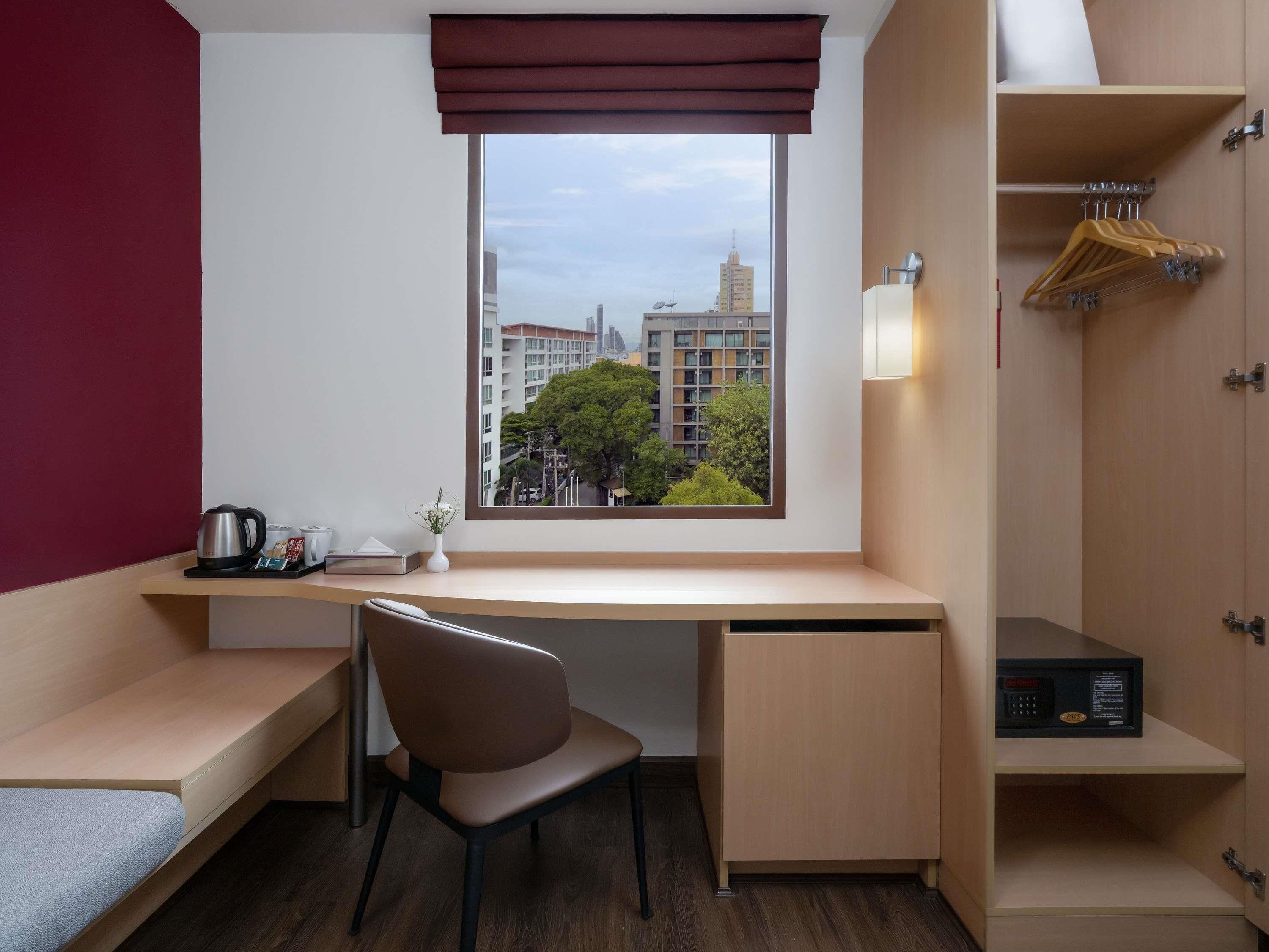 Ein kleines Hotelzimmer mit Schreibtisch, Stuhl und Blick auf die Stadt durch ein Fenster.