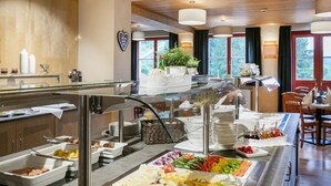 Un buffet proposant une variété de plats, notamment des viandes, des fromages et des légumes, dans une pièce bien éclairée, dotée d’un plafond en bois et de grandes fenêtres.