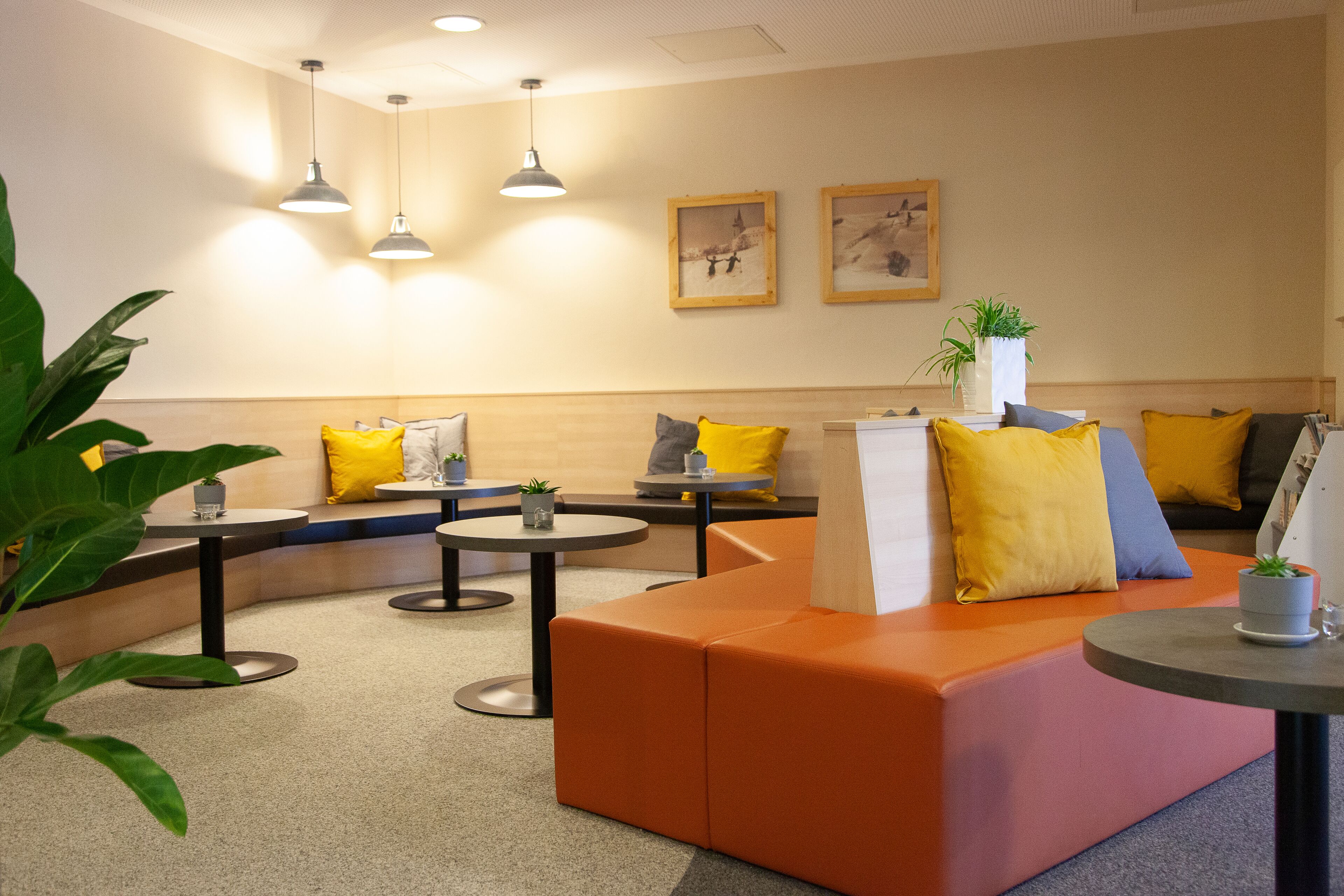 A modern waiting area with orange seating, round tables, and pendant lighting.