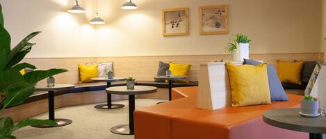 A modern waiting area with orange seating, round tables, and pendant lighting.