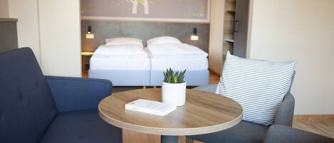 A hotel room with a bed, a blue sofa, a round wooden table with a plant, and a striped pillow.