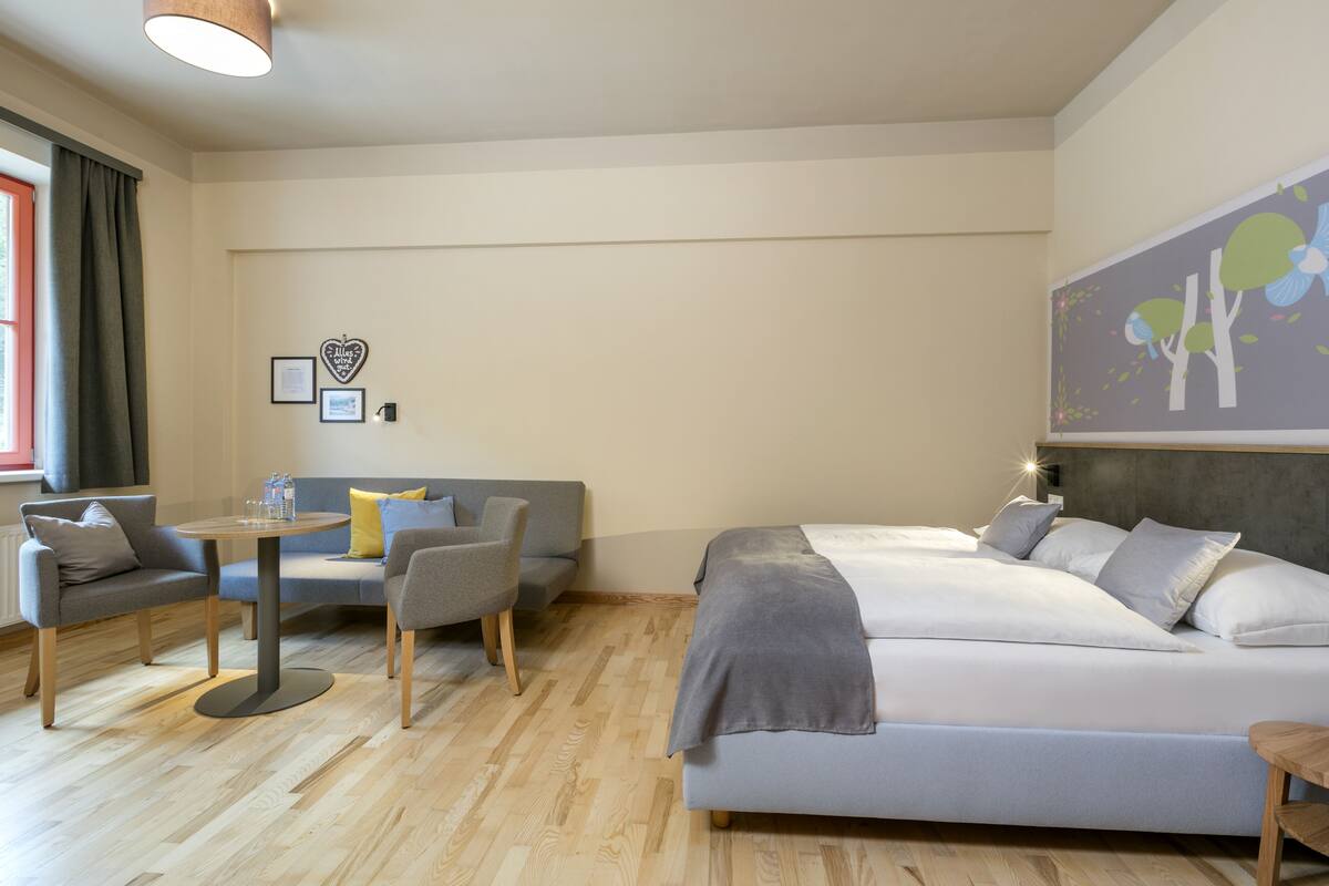 Une chambre moderne avec un lit, deux canapés, une petite table et une œuvre d’art murale.