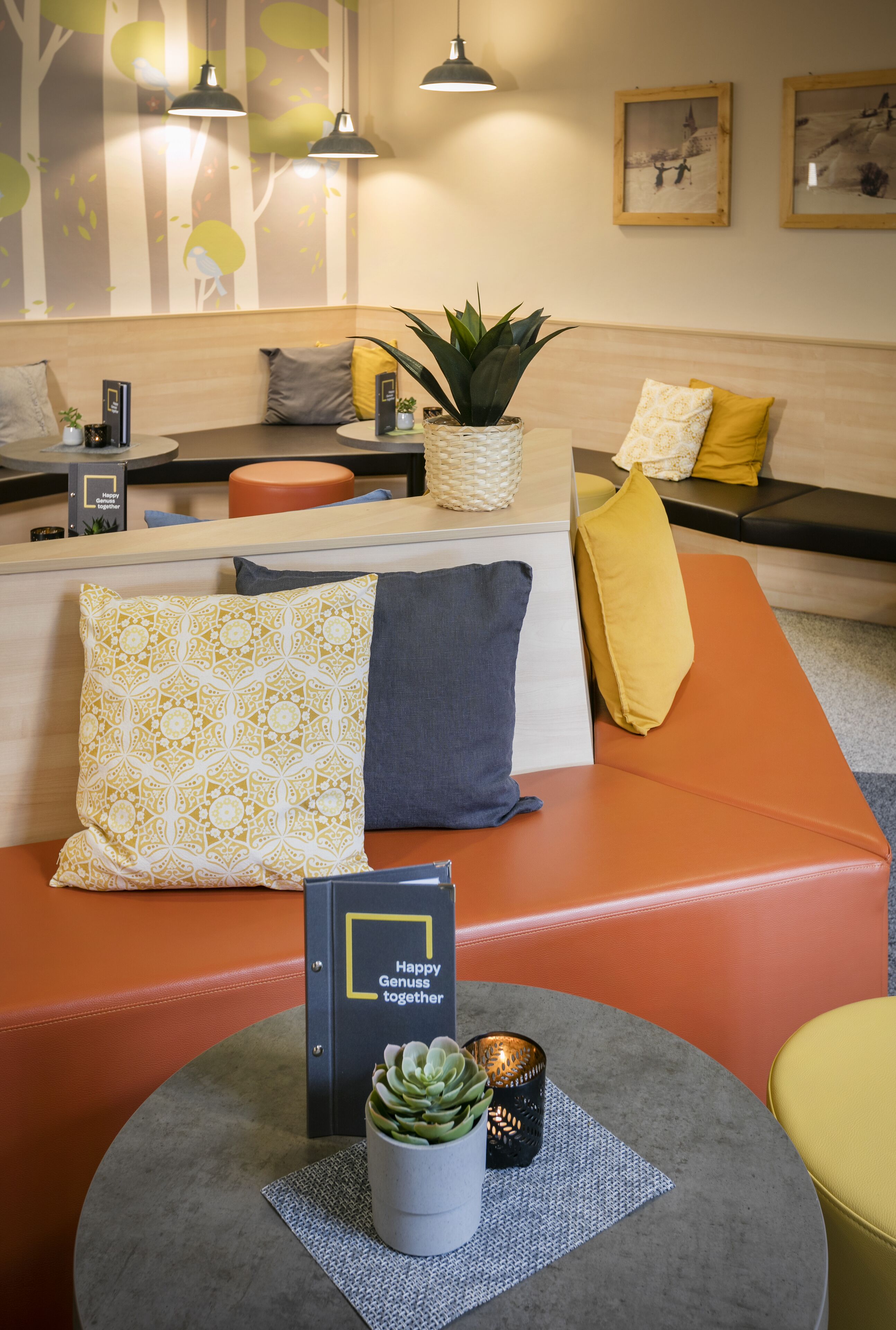 A modern reception area with a wooden reception desk, a seating area with orange and yellow cushions, and a potted plant.