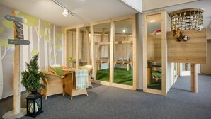 Une salle de jeux avec un filet d’escalade, un petit sapin de Noël, des fauteuils en osier et un panneau indicateur.