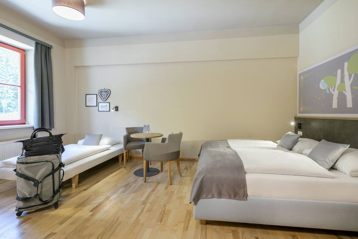 Une chambre d’hôtel équipée d’un lit, d’un bureau, d’une chaise, d’une petite table et d’un chariot à bagages.