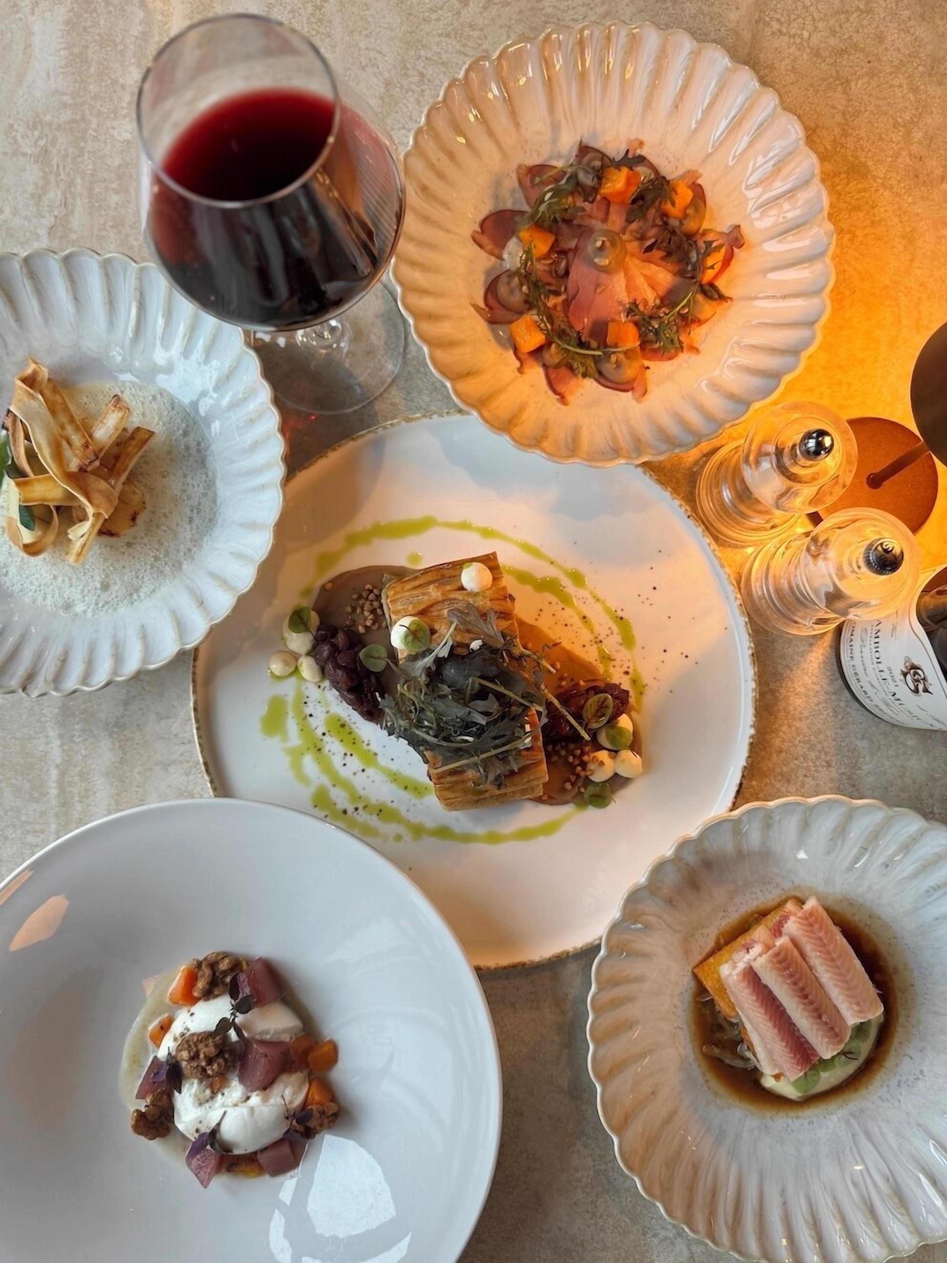 A table with various dishes, a glass of red wine, and a decorative salt shaker.