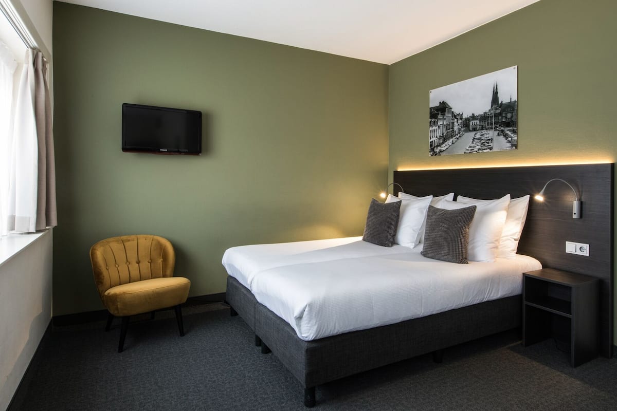 Una habitación de hotel con una cama, una silla, un televisor y una lámpara de pared.
