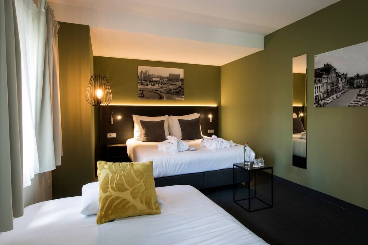 Una habitación de hotel con una cama grande, una mesita de noche, una lámpara y dos cuadros en la pared.