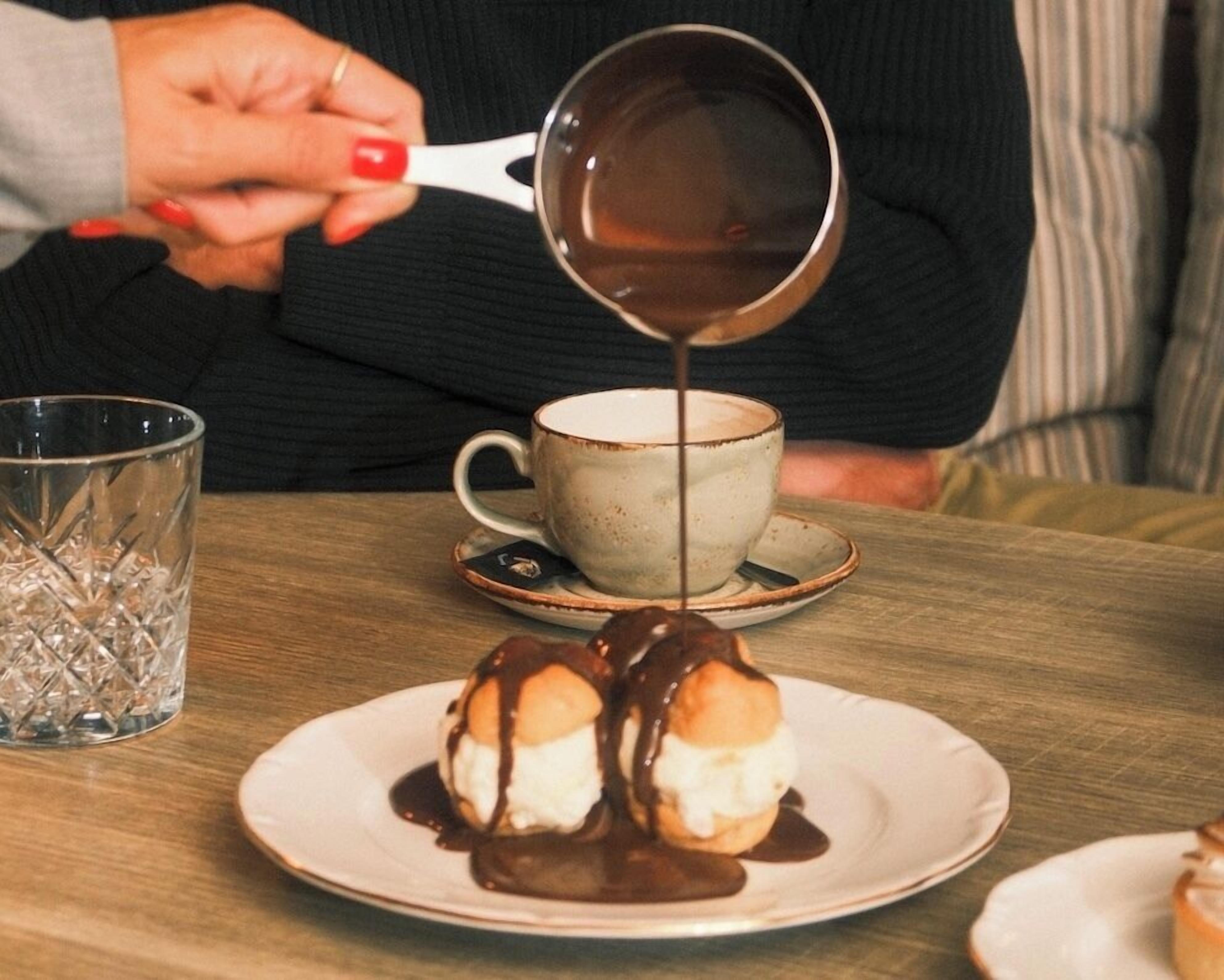A person pouring chocolate sauce over dessert on a plate.