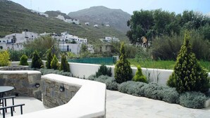 Un patio de piedra con una mesa redonda y sillas, rodeado de arbustos cuidadosamente recortados y una pequeña zona de piscina.