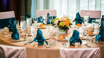 Een ronde tafel gedekt voor een formeel evenement, met netjes gerangschikt servies, gevouwen servetten en een bloemstuk als decoratie.