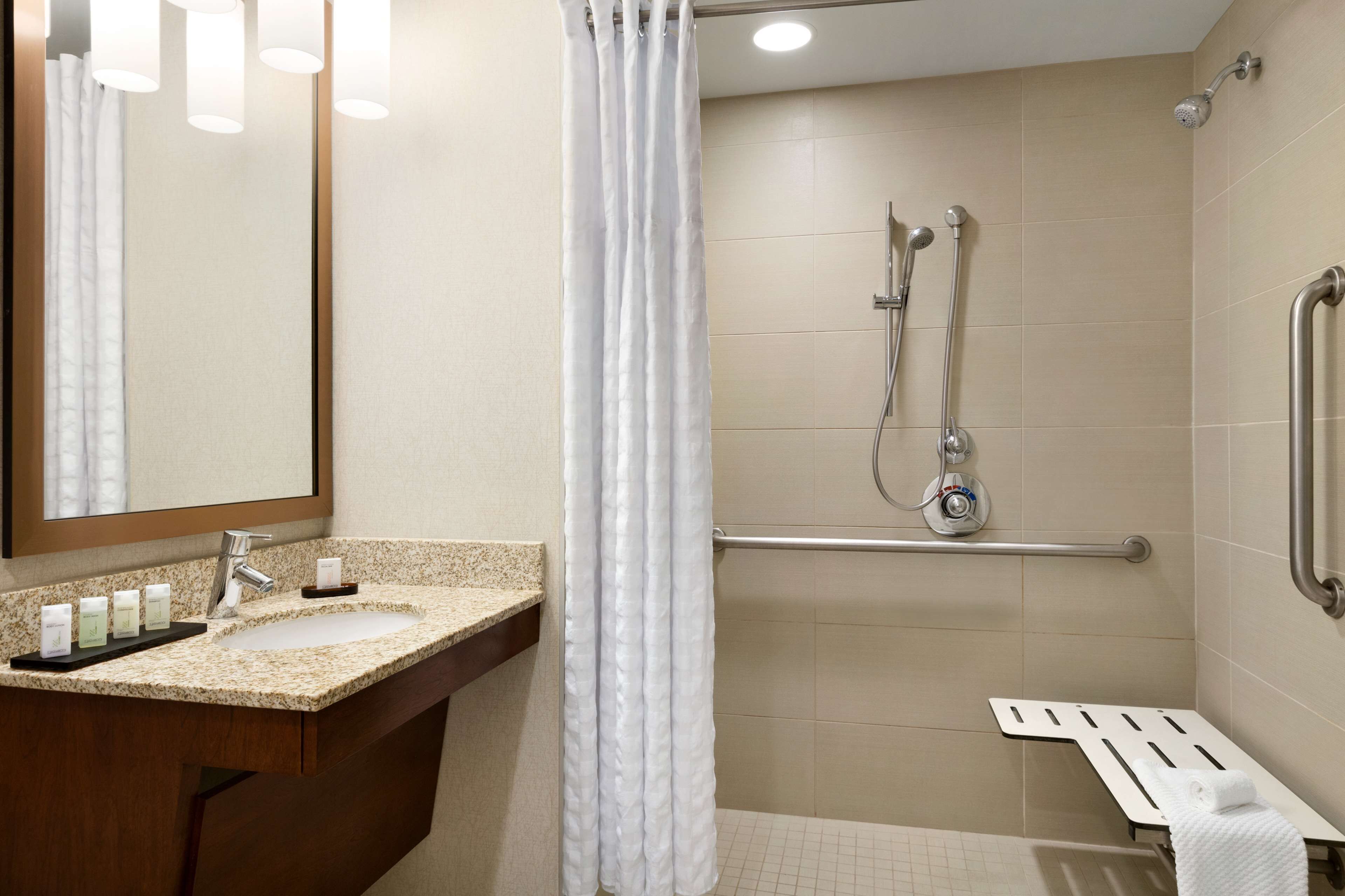 A bathroom with a sink, mirror, shower, and grab bars.